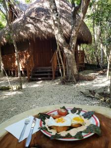 a plate of eggs and vegetables on a table in front of a hut at Aldea Maya-Ha Cabañas con cenotes in Puerto Morelos