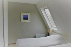 a white bedroom with a bed and a window at Appartement, Kaap 123 - Ameland in Hollum +21 photos