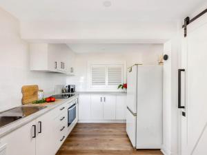 a white kitchen with white cabinets and a refrigerator at Blue View Gerringong in Gerringong