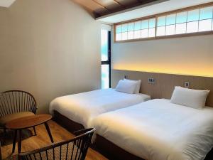 two beds in a room with a chair and a window at Kyomachirikyu Higashihonganji in Kyoto