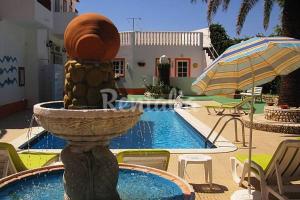 a fountain in front of a swimming pool with an umbrella at Palm Villa Estudios in Lagos
