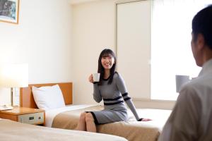 a woman sitting on a bed holding a cell phone at Kawasaki Central Hotel in Kawasaki
