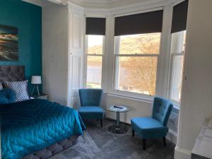 a bedroom with a bed and two blue chairs at Ashburn House in Fort William