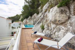 balcón con sillas blancas y pared de roca en Cala Galdana Apartamentos El Rio, en Cala Galdana