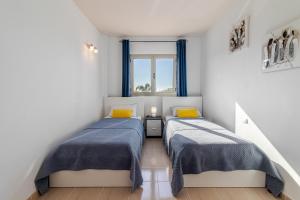 2 camas en una habitación blanca con almohadas azules y amarillas en Flatguest Trebolina - 3Bdr - FastWiFi - Parking, en Vecindario