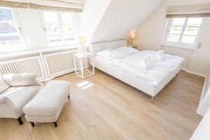 a white bedroom with a bed and a chair at Landhaus Tinnumburg in Westerland (Sylt)
