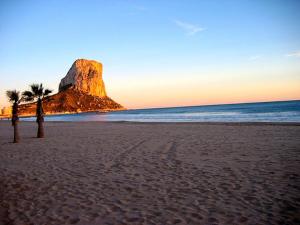 a beach with a rock and palm trees and the ocean at Sol y Mar in Calpe