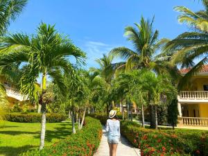 a woman walking down a path in front of palm trees at La Ensenada Beach Resort in Tela