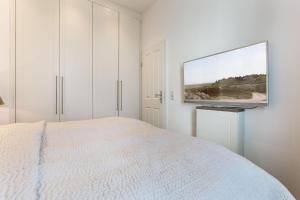 ein weißes Schlafzimmer mit einem Bett und einem TV an der Wand in der Unterkunft Art your Life Residenz Seeburg Whg 8 in Westerland