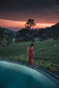 une femme en robe rouge debout à côté d'une piscine dans l'établissement Samanvaya - Adults Only, à Sidemen