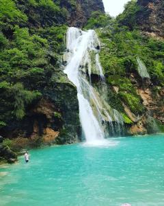 a man standing in the water in front of a waterfall at G R A N D C H A L E T in Salalah