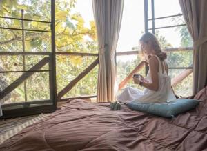 Una chica sentada en una cama mirando por la ventana en Baansuan Chomchun en Amphoe Mae Taeng