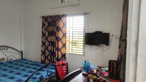 Dormitorio con cama, escritorio y TV en Vamoose Murti Homestay, en Chālsa Mahābāri