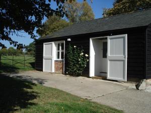 a small black building with white doors and a driveway at Stable Cottage - Milton Lilbourne in Pewsey