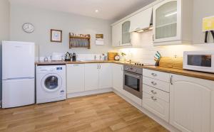 cocina con armarios blancos, lavadora y secadora en Stable Cottage - Milton Lilbourne, en Pewsey