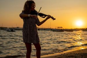 a woman playing a violin on the beach at sunset at Hostal la Savina in La Savina