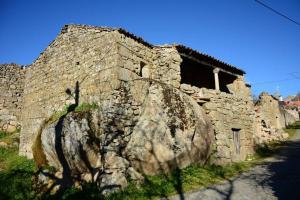 a stone building with a large rock next to a street at Villa Tauria- Casa de campo em aldeia medieval in Sabugal