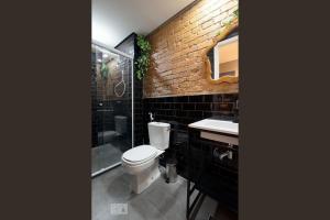 uma casa de banho com um WC, um lavatório e uma parede de tijolos em A CASINA - STUDIOS Metrô FARIA LIMA em São Paulo