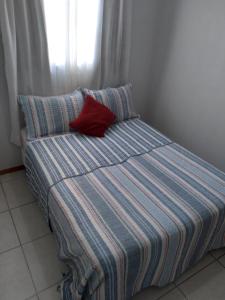 a bed with a red pillow and a window at apartamento com piscina in Piçarras