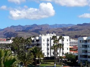 a white building with palm trees and mountains in the background at Taidia Sunset View in Playa del Ingles