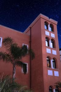 a red building with a palm tree next to it at Artemis Hotel in Cefalù