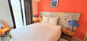a bedroom with a white bed with an orange wall at Appart'Hôtel du Bout du Monde in Camaret-sur-Mer