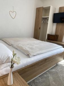 a bed with white sheets and a vase with a flower at Genussgasthof Fuldaquelle & Berghof Wasserkuppe in Gersfeld