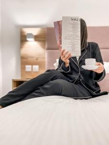 a woman laying on a bed reading a book and holding a cup of coffee at Hypnos Boutique Hotel in Nicosia