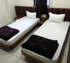 Duas camas num quarto com lençóis brancos e almofadas castanhas em Hotel Milan em Ahmedabad