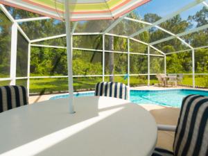 a table with chairs and an umbrella next to a swimming pool at Sunshine, Love, And Happiness In A Home Thats Cute As A Button - 3bd 2552 in Kissimmee