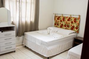 um pequeno quarto com uma cama branca e uma cómoda em Pousada Recanto do Lago 1 em Capitólio