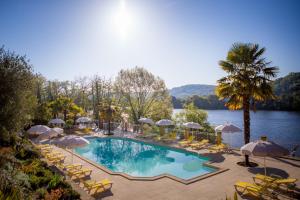 ein Swimmingpool mit Stühlen und Sonnenschirmen neben einem See in der Unterkunft Les Magnolias in Lalinde