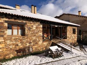 une maison en pierre avec des chaises et une terrasse couverte dans la neige dans l'établissement El Hayuco de Montejo, à Montejo de la Sierra