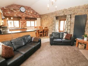 a living room with a leather couch and a kitchen at Fletchers Barn in Alderwasley
