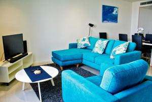 a living room with a blue couch and a tv at Absolute Waterfront - Tropical Sunrise Apartment Over The Water in Darwin