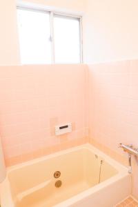 een badkamer met een bad en roze tegels bij HAT Kujo, near from Kintetsu Kujo station 近鉄九条駅前の民泊 in Kōriyama