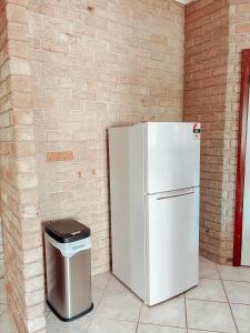 a white refrigerator and a trash can next to a brick wall at Carnarvon 3BR & 2BA Holiday House in Carnarvon