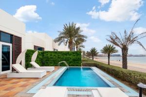 a swimming pool with two white chairs next to a beach at FAM Living - Sarai Beachfront Villas - 2 in Dubai