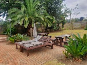 un patio con bancos, mesas y una palmera en SM Africa Guest House, en Alberton