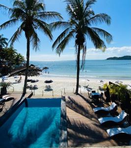 a swimming pool next to a beach with palm trees at Pousada Castellammare in Bombinhas