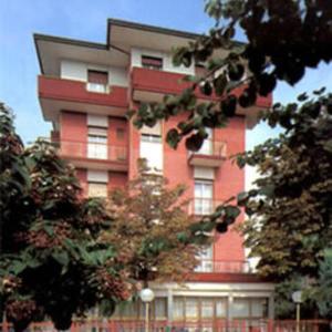 un alto edificio rojo con árboles delante de él en HOTEL ROSSINI, en Rímini