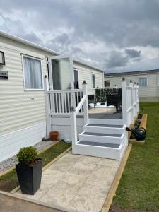 un porche con barandilla blanca y escaleras junto a una caravana en Hutchinson's Willerby Kelston with Hot tub en Cottom