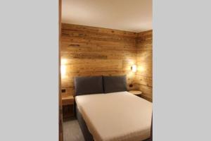 1 dormitorio con cama blanca y pared de madera en Snowflake Apartment - Livigno, en Livigno