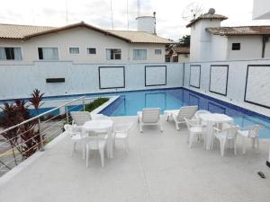un patio con mesas blancas y sillas junto a una piscina en apartamento 2 quartos em Porto segur BA, en Porto Seguro