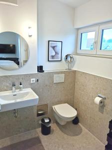 ein Badezimmer mit einem Waschbecken, einem WC und einem Spiegel in der Unterkunft MAISON AMAND - Am See mit Privatstrand in Immenstaad am Bodensee