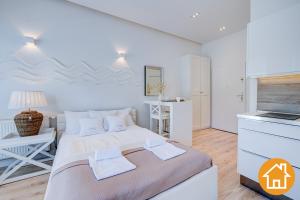 a white bedroom with a large bed and a kitchen at Apartamenty Marea - visitopl in Międzyzdroje