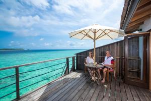 
two women sitting on a wooden bench under an umbrella at Reethi Beach Resort in Baa Atoll
