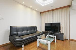 een woonkamer met een zwarte leren bank en een tv bij Mon Petit Chat in Kanazawa