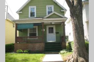 een groen huis met een veranda en een boom bij The Oakwood Cottage- With Private Yard & Parking, Minutes From Falls & Casino by Niagara Hospitality in Niagara Falls