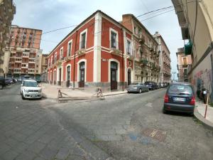 ein rotes Gebäude auf einer Stadtstraße mit parkenden Autos in der Unterkunft Strange Apartament in Catania